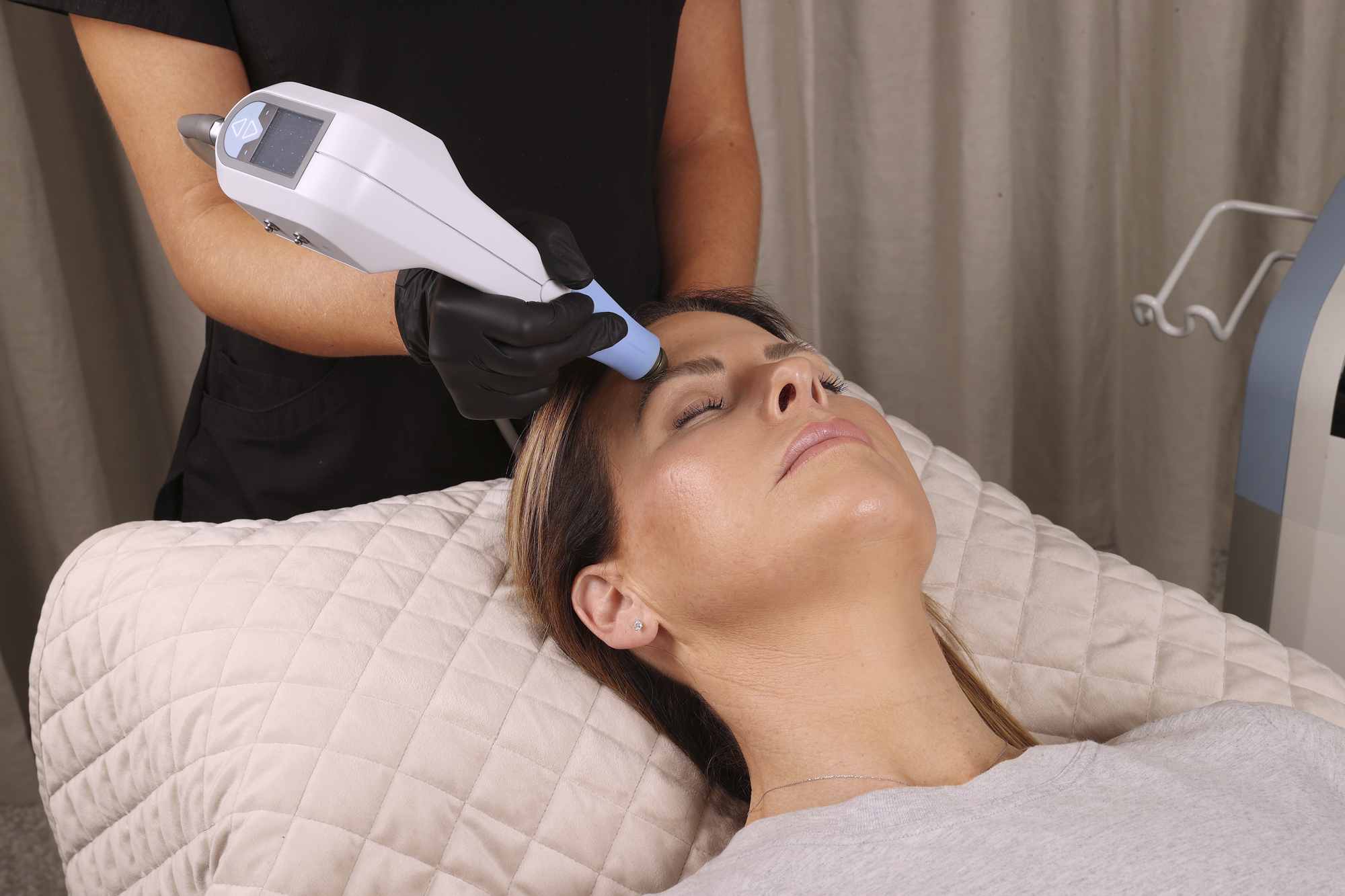 Woman receiving a facial treatment with a device held by a professional in a clinical setting.
